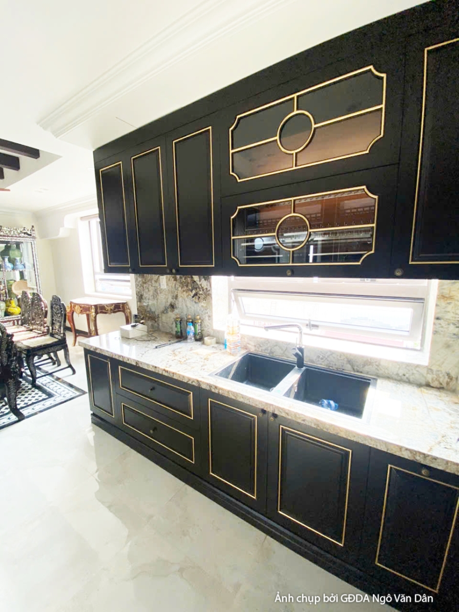 Tủ bếp dưới màu đen với mặt bàn đá sáng, bồn rửa và vòi nước hiện đại. Không gian bếp được thiết kế tối giản, tập trung và…