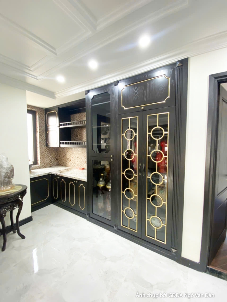 Tủ bếp trên dưới màu đen với chi tiết viền vàng, mặt bàn đá sáng màu. Không gian bếp được thiết kế đồng bộ, mang lại vẻ đẹ…