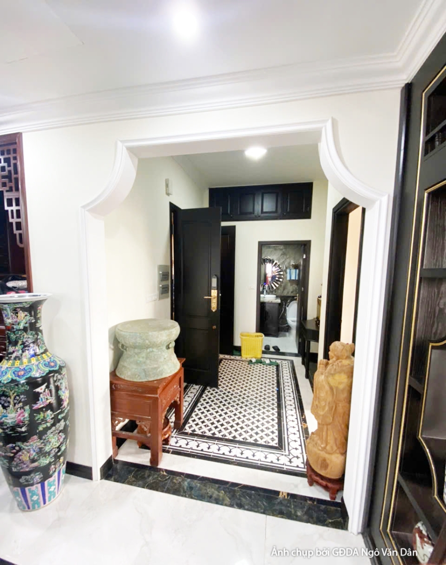 Hành lang hoặc lối đi với tủ trưng bày gỗ tối màu, sàn gạch hoa văn đen trắng. Không gian được trang trí với các vật phẩm…