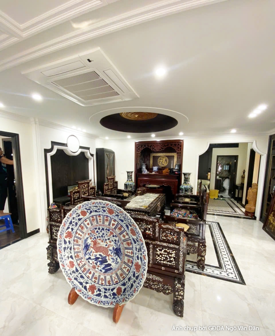Góc nhìn khác của phòng khách, thể hiện sự hài hòa giữa bộ bàn ghế gỗ truyền thống và tủ kệ trang trí hiện đại. Sàn gạch h…