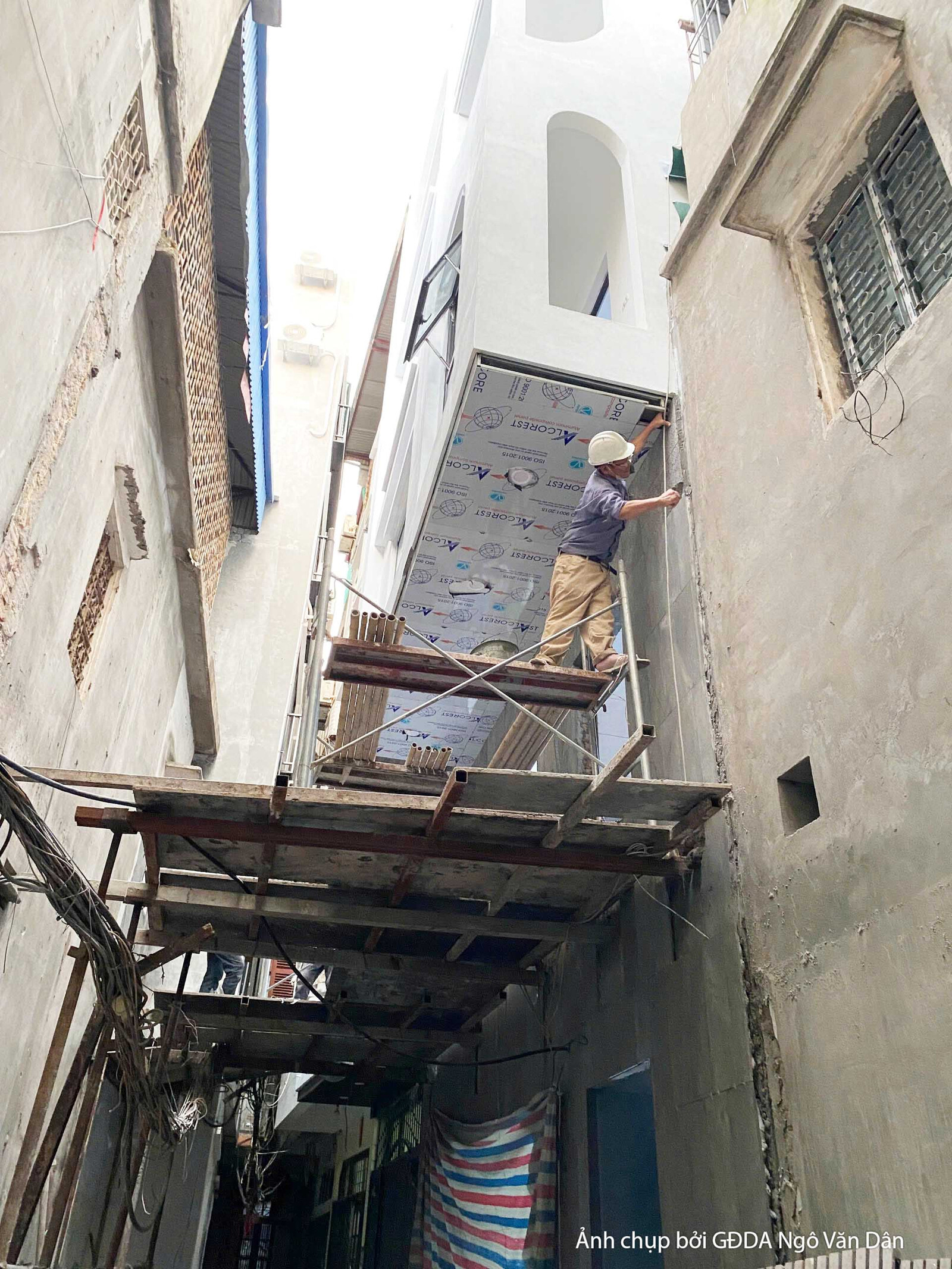 Công nhân đang thực hiện công việc trên giàn giáo tại mặt tiền công trình, tập trung vào việc hoàn thiện các chi tiết xây…