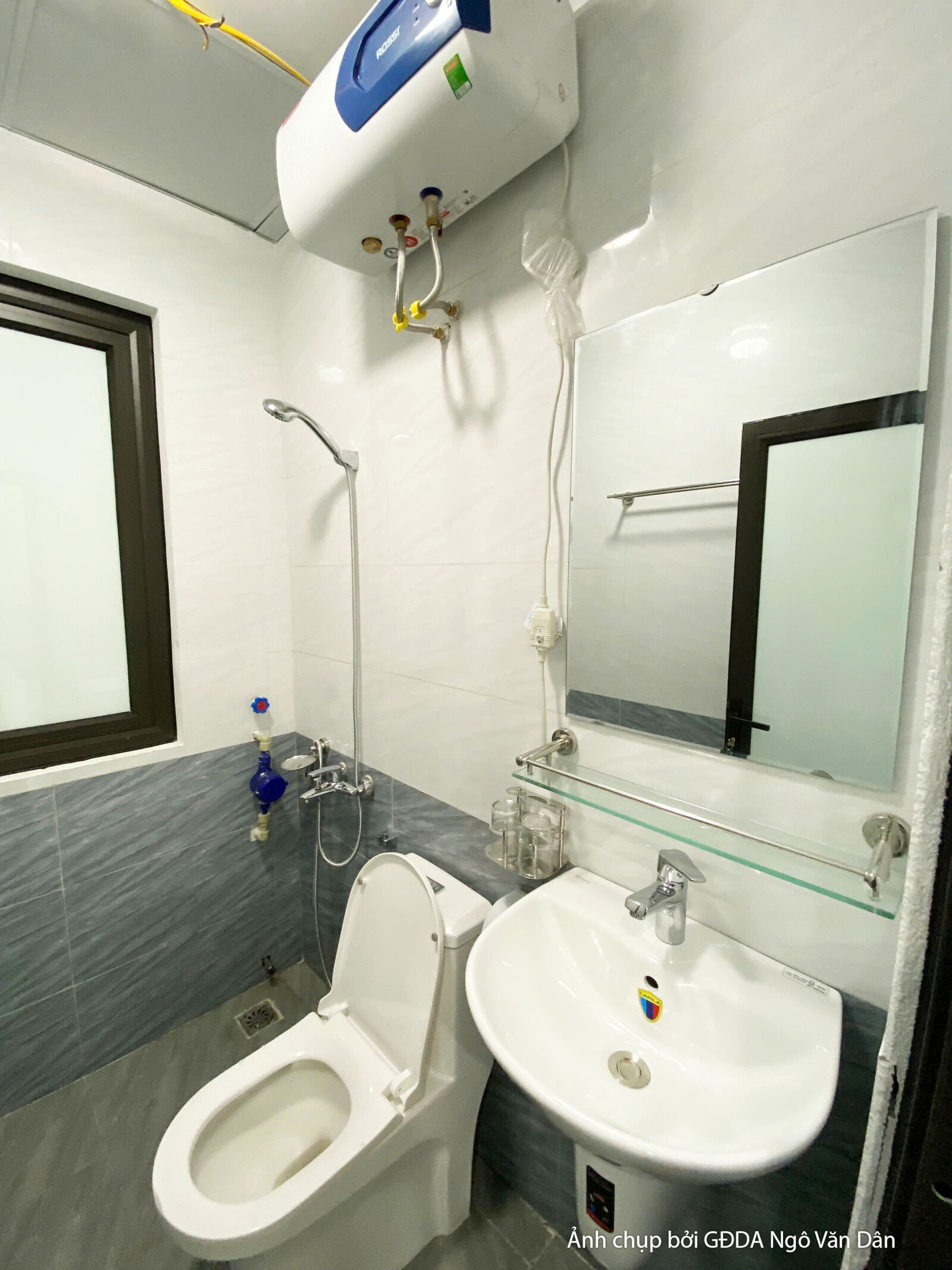 Nhà vệ sinh đã hoàn thiện với bồn cầu, lavabo, gương treo tường và bình nóng lạnh. Gạch ốp tường màu xám kết hợp gạch sàn…