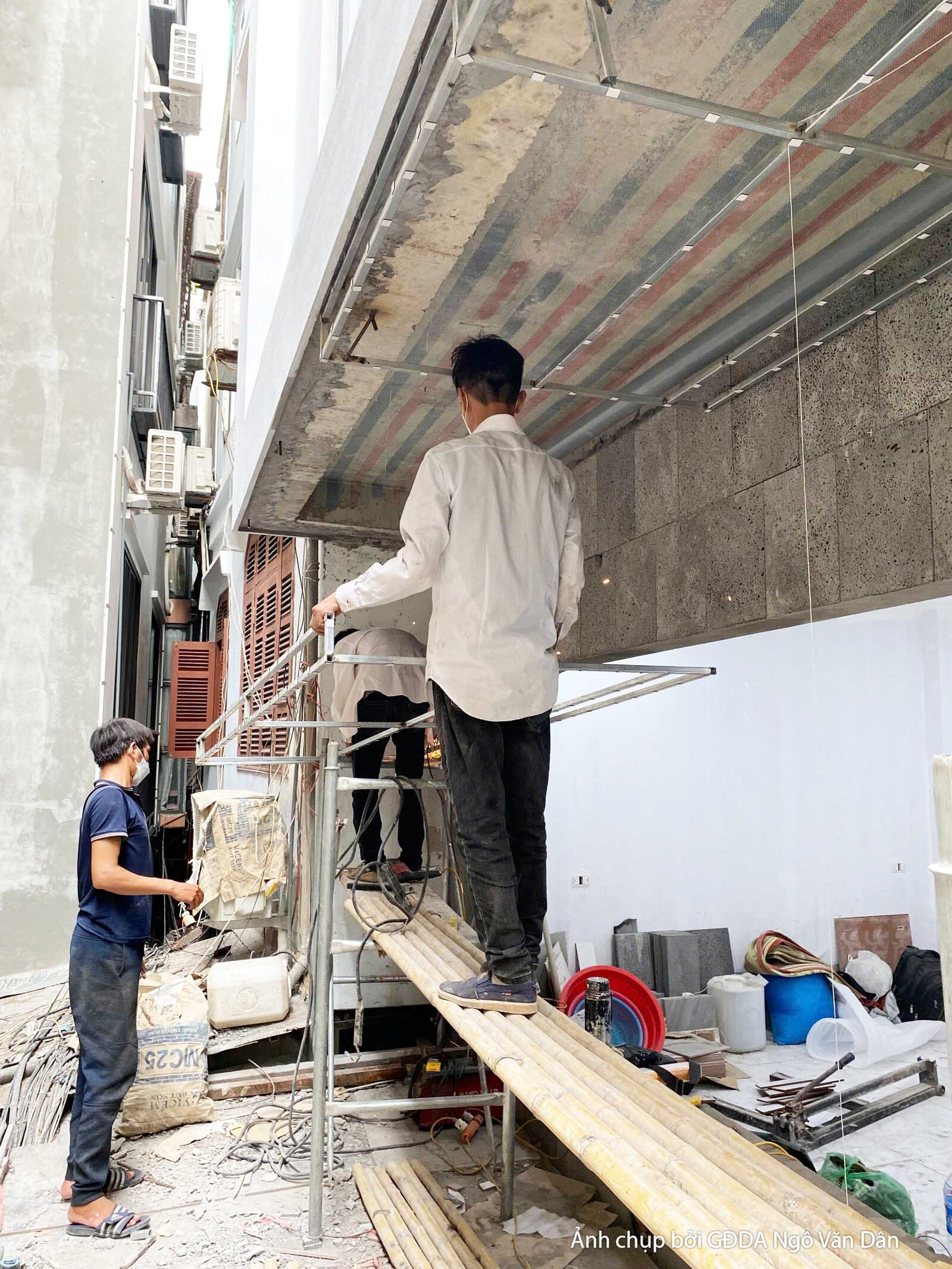 Công nhân đang vận chuyển các tấm ván gỗ dài vào bên trong công trình, chuẩn bị cho giai đoạn thi công nội thất. Bố cục từ…