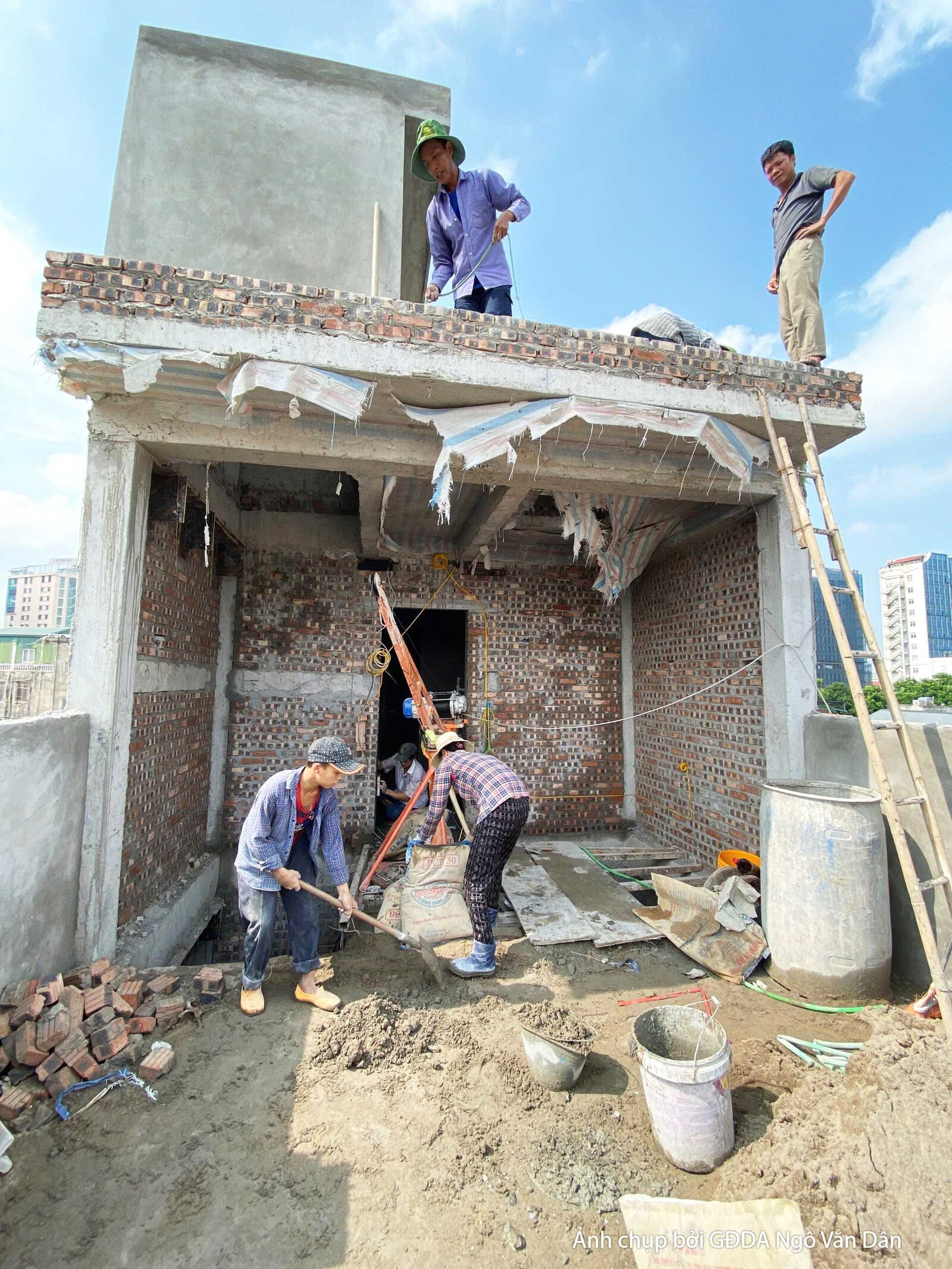 Công nhân đang trộn vữa hoặc xi măng tại khu vực sân thượng hoặc tầng mái, chuẩn bị cho các công đoạn hoàn thiện. Bố cục t…