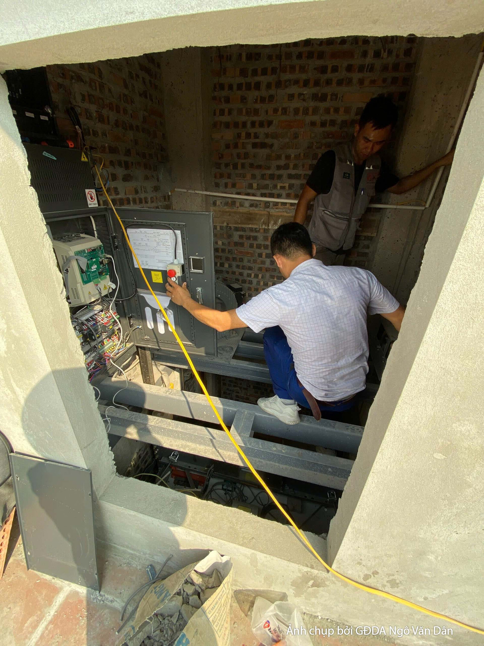 Không gian đang trong quá trình lắp đặt hệ thống kỹ thuật và điện. Bố cục từ góc nhìn ngang cho thấy một công nhân đang là…