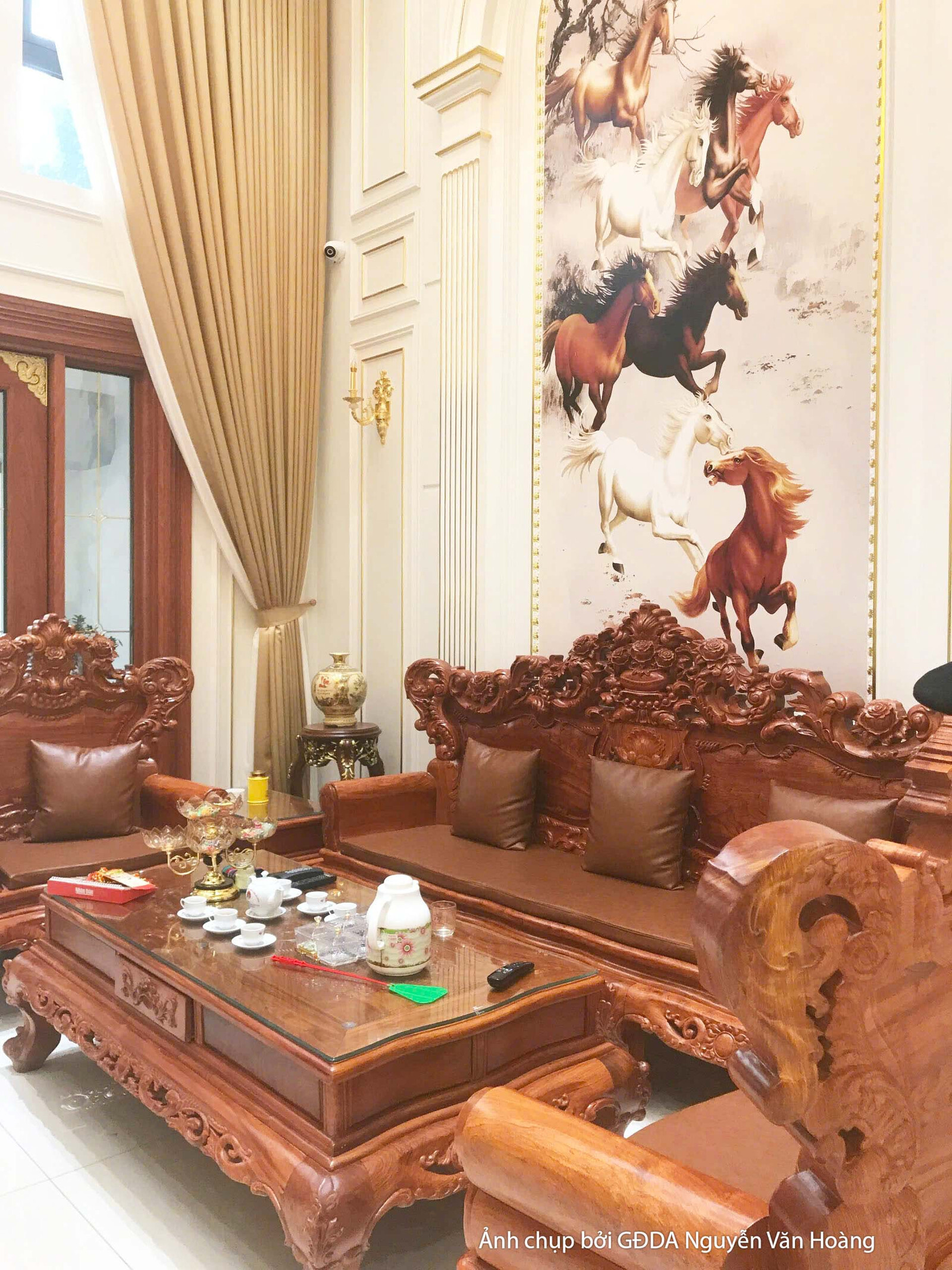 Cận cảnh bộ sofa gỗ tự nhiên chạm khắc tinh xảo trong phòng khách. Rèm cửa màu nâu vàng sang trọng, kết hợp với tranh nghệ…