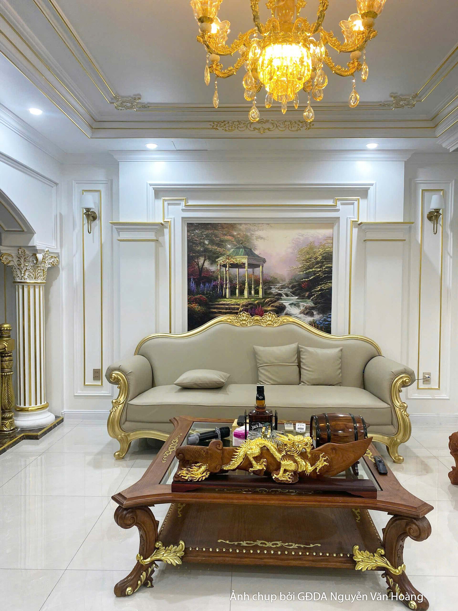 Không gian phòng khách phụ hoặc sảnh sinh hoạt chung trên tầng, với bộ sofa tân cổ điển màu kem và bàn trà gỗ. Đèn chùm ph…