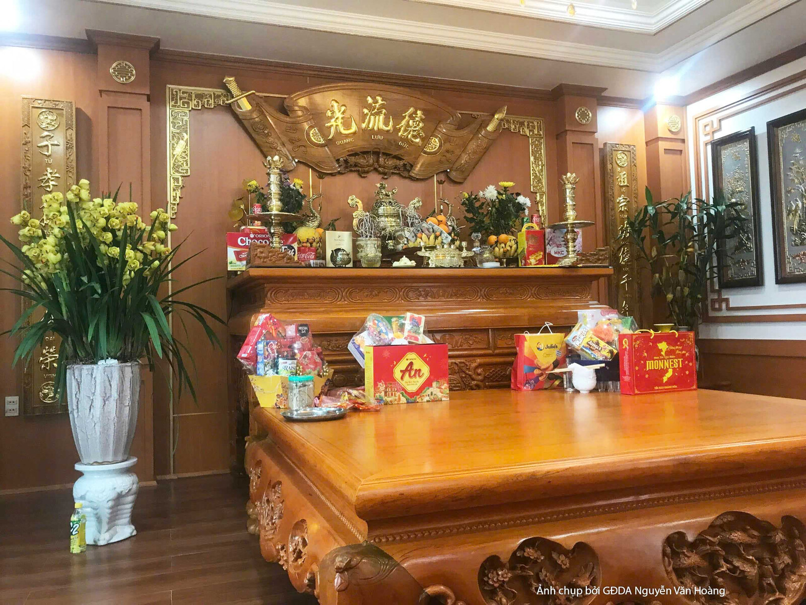 Cận cảnh không gian trang trọng, nổi bật với tủ gỗ chạm khắc tinh xảo và bàn gỗ lớn. Các vật phẩm trang trí được sắp xếp g…