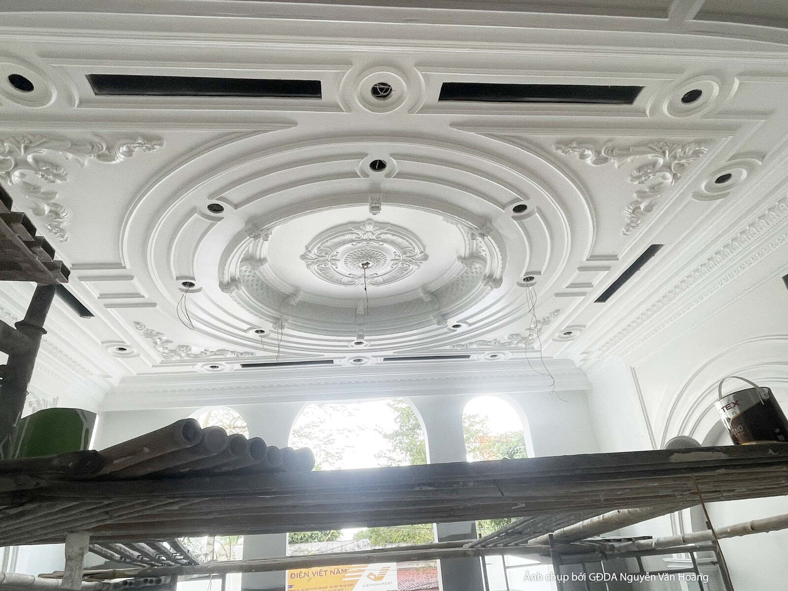 Cận cảnh trần thạch cao đang trong giai đoạn lắp đặt, với các họa tiết phào chỉ tròn và đường nét trang trí phức tạp. Giàn…
