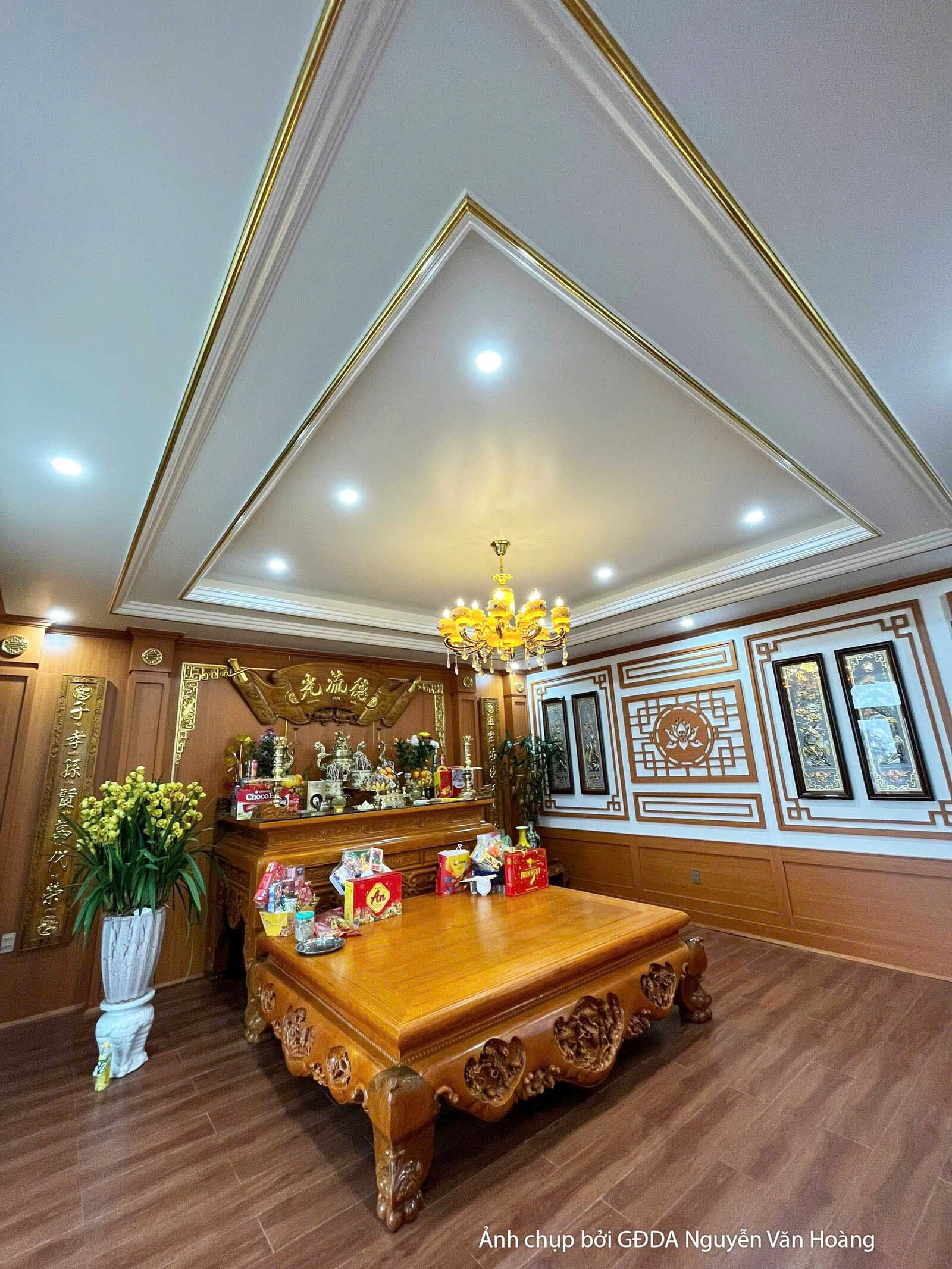 Không gian trang trọng với tủ gỗ chạm khắc tinh xảo, bàn gỗ lớn đặt giữa phòng. Trần thạch cao giật cấp với đèn âm trần và…