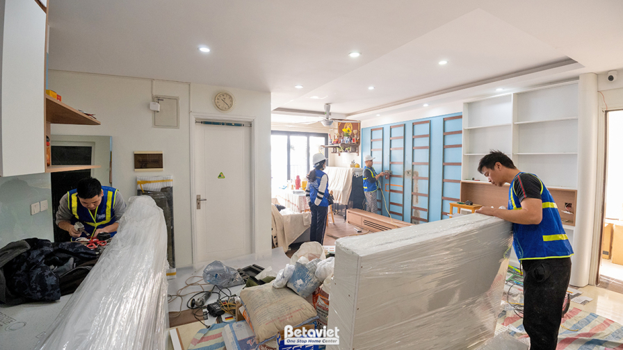 Cận cảnh khu vực cửa ra vào và hành lang, nơi các tủ kệ giày hoặc tủ trang trí đang được lắp đặt. Các vật liệu gỗ công ngh…