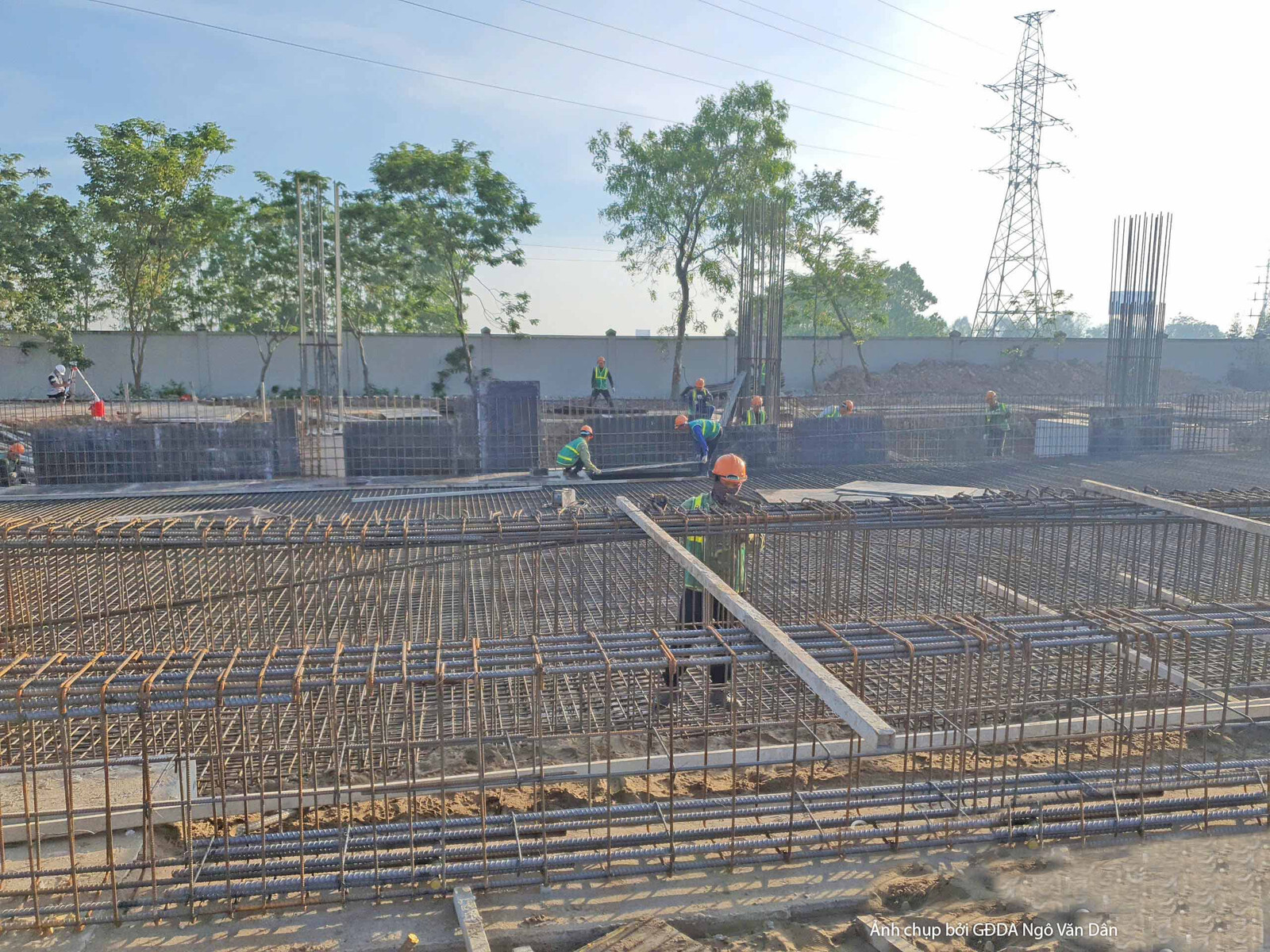 Công nhân đang lắp dựng cốt thép cho hệ sàn hoặc dầm, với các thanh thép được sắp xếp theo dạng lưới. Bố cục rộng, cho thấ…