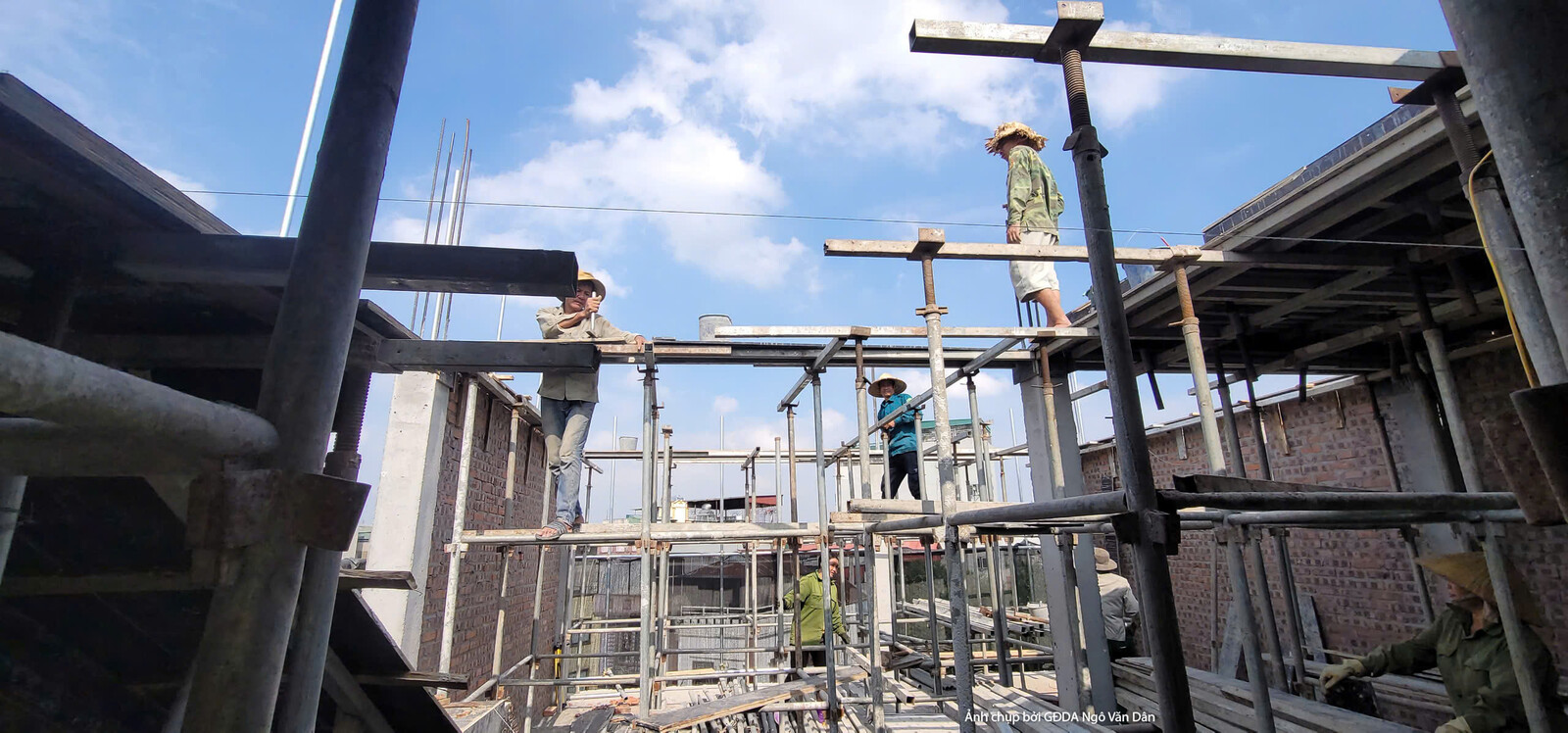Công nhân đang làm việc trên hệ thống giàn giáo gỗ tạm thời, thực hiện các công đoạn xây dựng phần mái hoặc kết cấu tầng t…