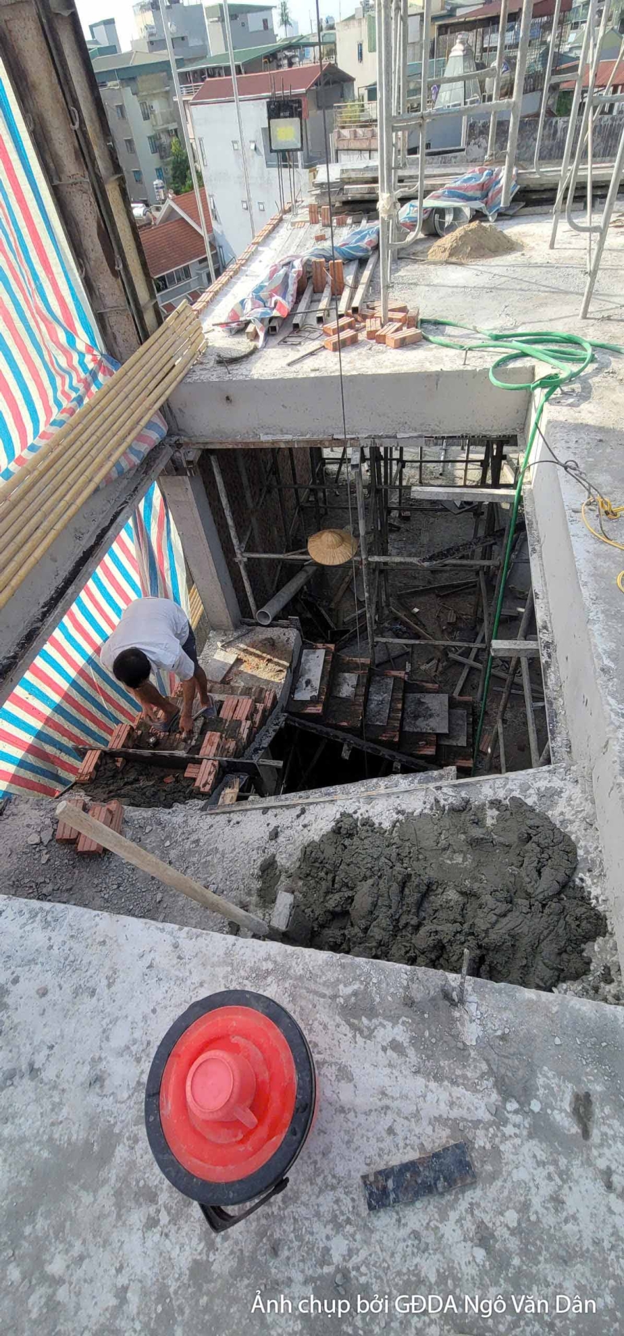Công nhân đang làm việc dưới hố móng hoặc khu vực nền, thực hiện các công đoạn chuẩn bị hoặc xử lý vật liệu. Đất và vật li…