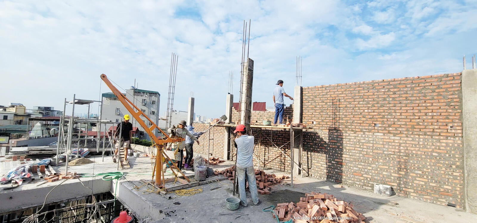 Góc nhìn từ trên cao xuống công trường thi công phần thô, cho thấy rõ các bức tường gạch đỏ cam đang được xây dựng và hệ t…