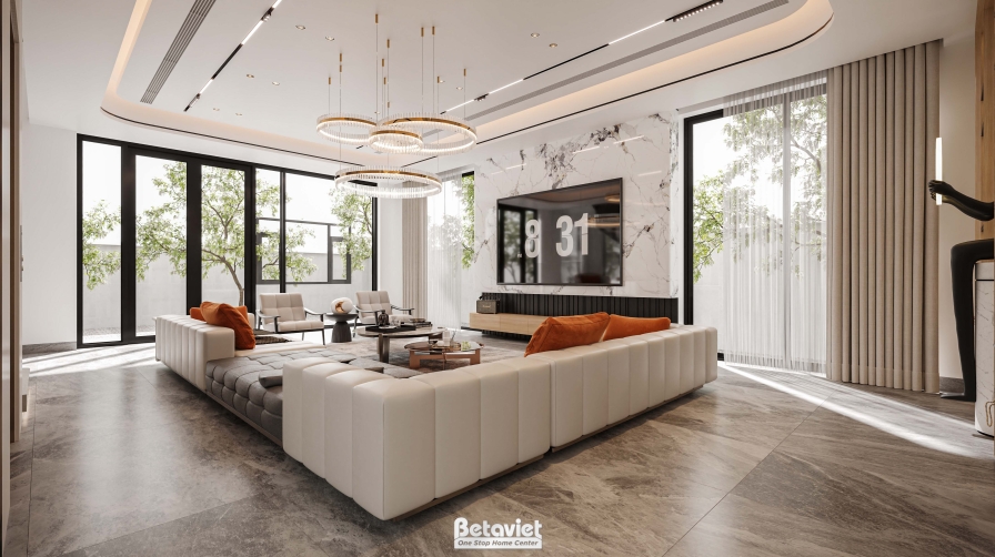 Phòng khách nhìn từ hướng cửa kính ra vườn, sofa góc chữ L bọc da màu kem dáng bọc nệm múi, sàn gỗ xương cá. Hệ đèn thả vò…