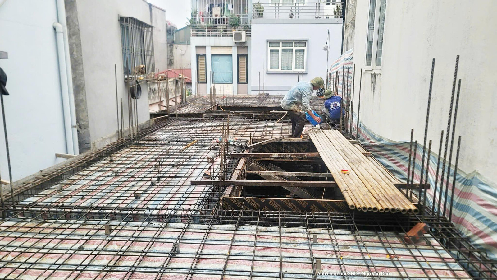 Công trường thi công phần thô, nhìn từ trên cao xuống khu vực sàn tầng. Các công nhân đang làm việc trên giàn giáo, chuẩn…