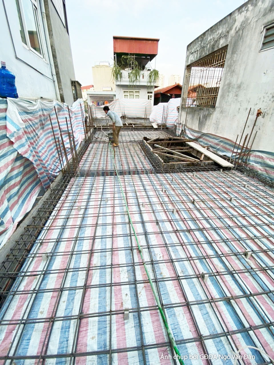 Sàn thép chờ đổ bê tông tại tầng thượng, nhìn dọc hành lang hẹp giữa các dãy nhà liền kề. Lưới thép buộc chắc, phủ bạt sọc…