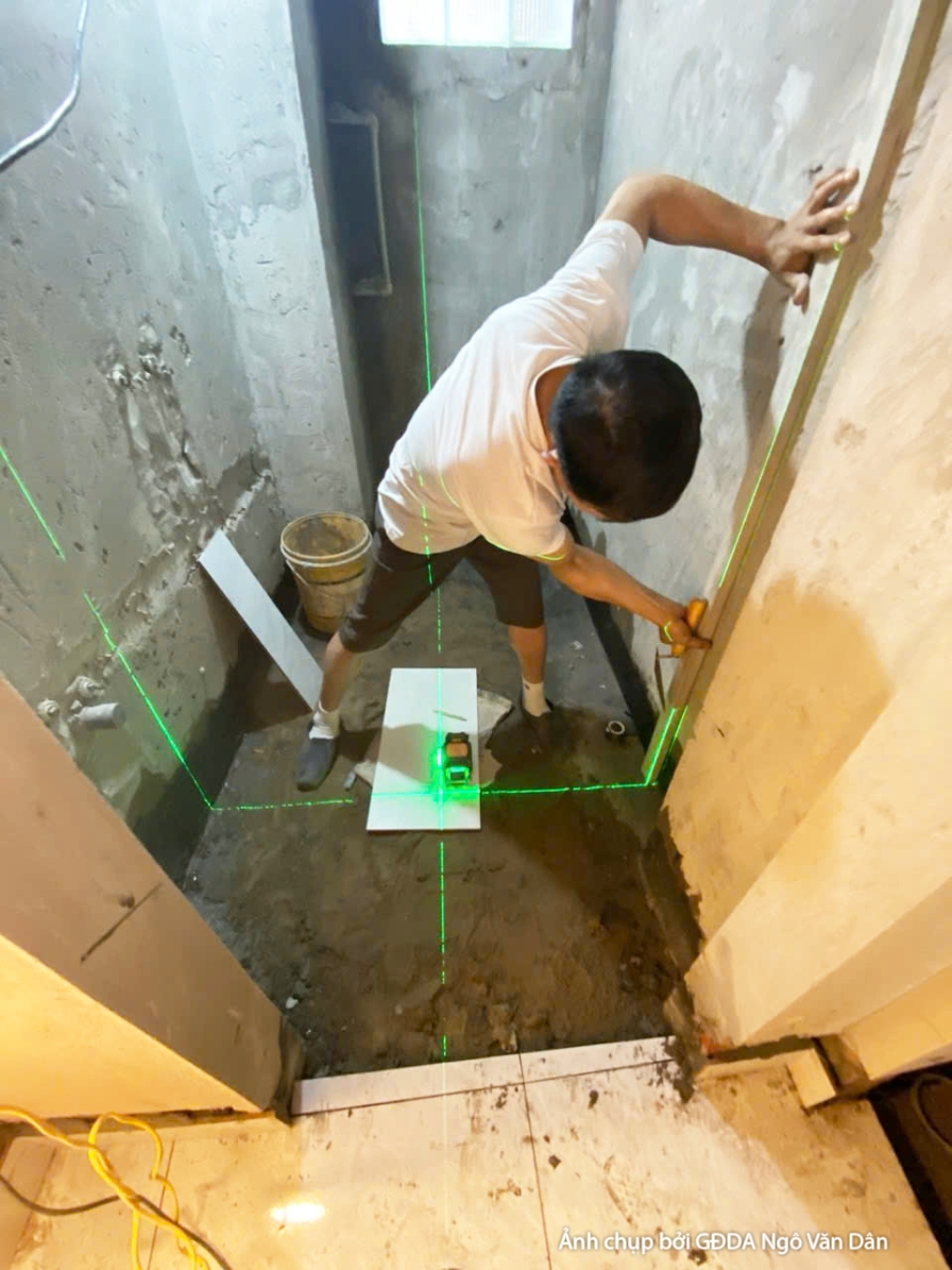 Công nhân đang kiểm tra và định vị các chi tiết kỹ thuật trên sàn bê tông bằng thiết bị laser. Ánh sáng xanh của tia laser…