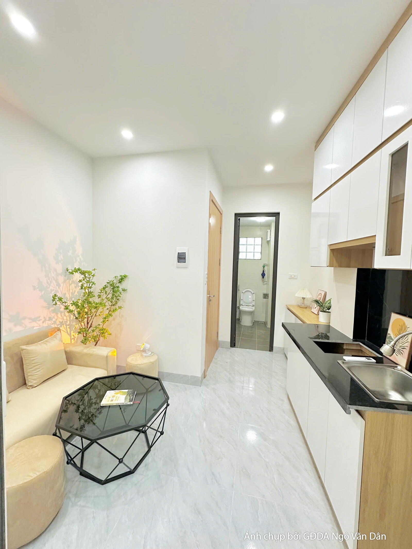 Không gian bếp và phòng khách liên thông của căn hộ đã hoàn thiện, nhìn từ khu bếp bao quát ra cửa chính và hành lang dẫn…