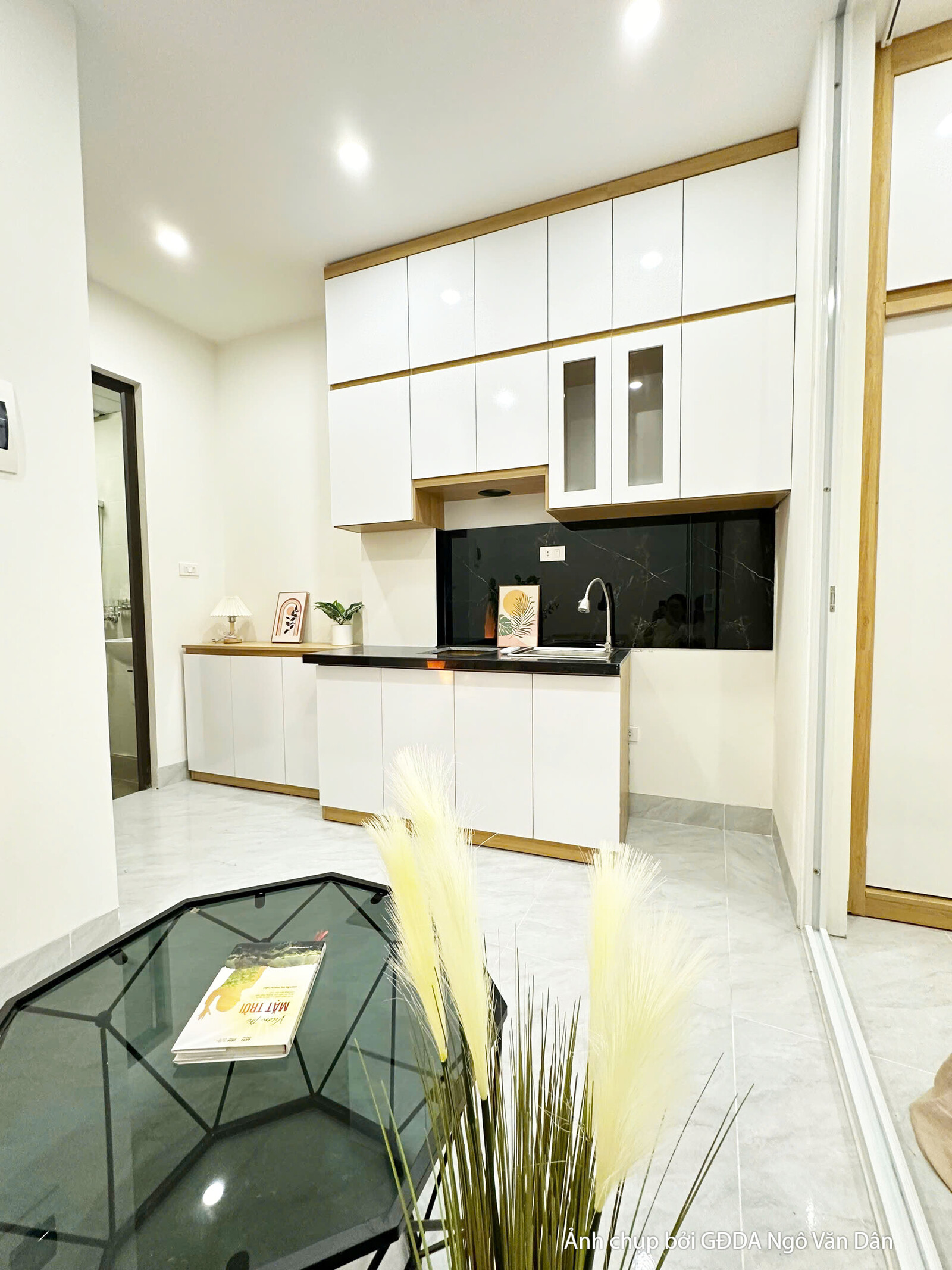 Không gian phòng khách và ban công của căn hộ chung cư mini đã hoàn thiện, nhìn từ góc phòng khách. Sofa màu be, bàn trà t…
