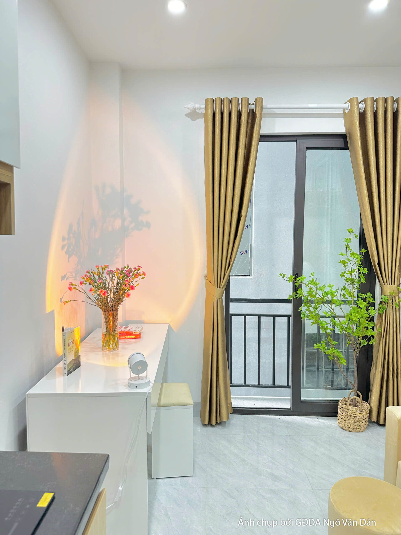 Không gian phòng khách và bếp của căn hộ chung cư mini đã hoàn thiện, nhìn từ góc bếp. Tủ bếp trên dưới màu trắng và vân g…