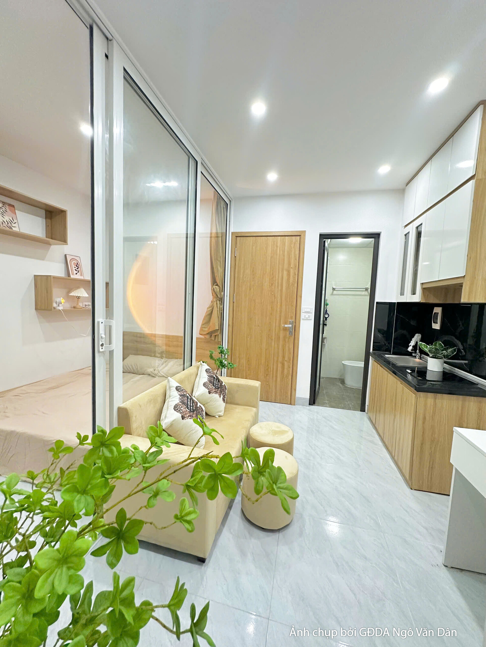 Không gian phòng khách kết hợp bếp của căn hộ hoàn thiện, nhìn từ góc vách kính ngăn phòng ngủ hướng ra phía bếp. Sofa be…