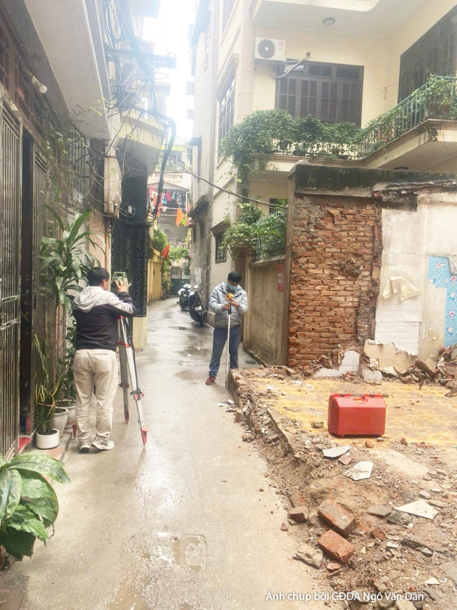 Công trường thi công phần thô, nhìn từ góc đường hẹp vào bên trong công trình. Các bức tường gạch cũ của công trình lân cậ…