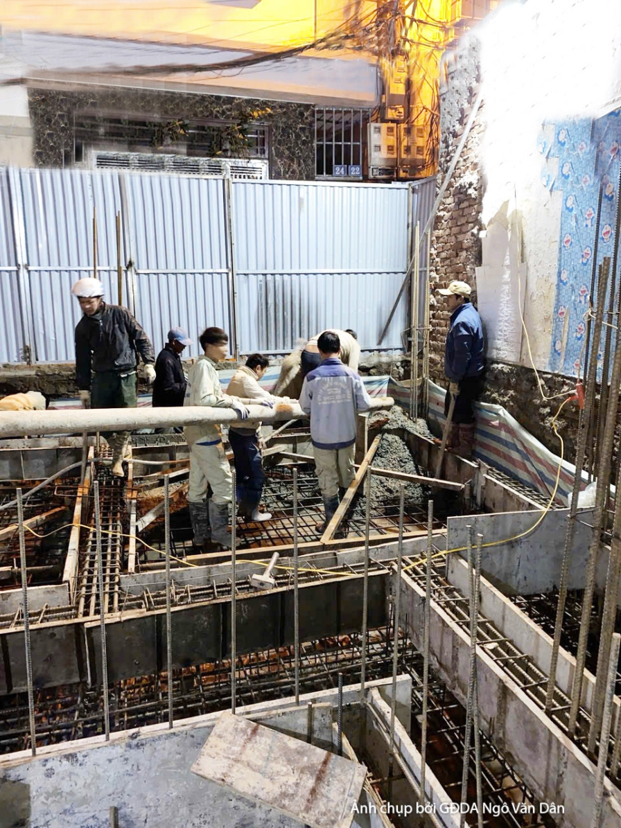 Công trường thi công phần thô, nhìn từ trên cao xuống khu vực móng và tầng trệt. Các công nhân đang làm việc với sắt thép…
