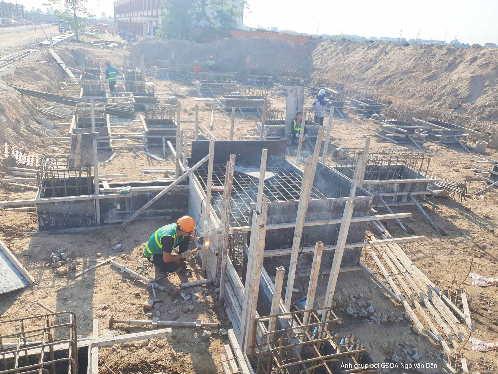 Góc nhìn cận cảnh khu vực thi công móng cọc và đài móng. Nhiều công nhân đang làm việc trong hố móng sâu, lắp đặt cốt thép…