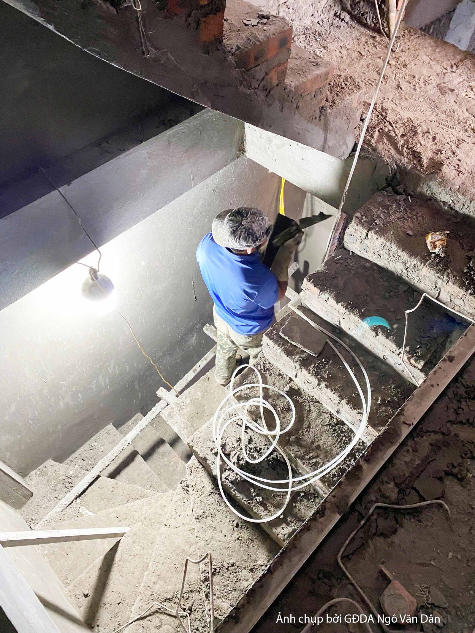 Cầu thang bộ đang trong giai đoạn thi công phần thô, với các bậc thang bê tông chưa hoàn thiện. Một công nhân đang làm việ…