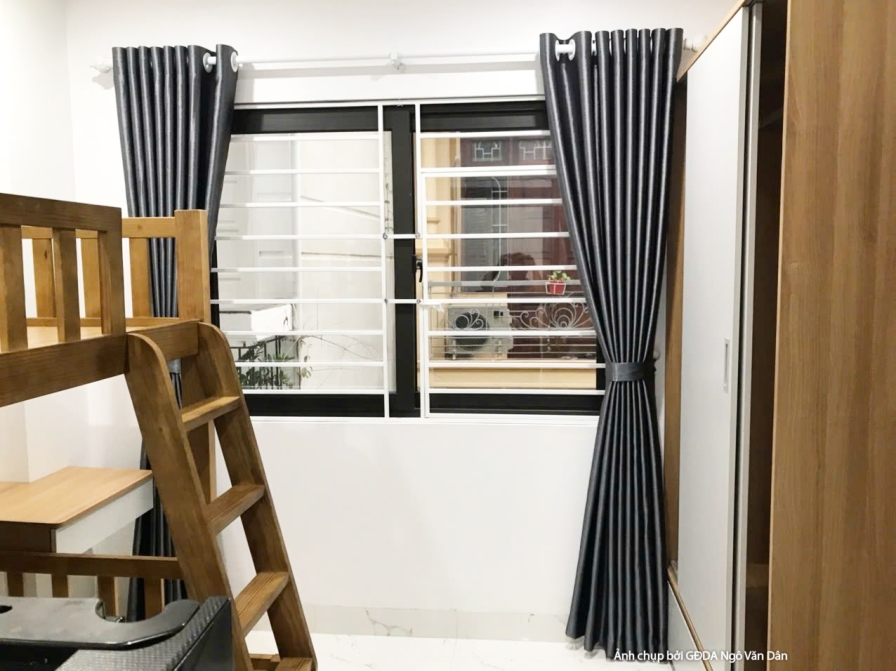 Không gian phòng ngủ nhỏ với giường tầng gỗ, tủ quần áo cánh trắng vân gỗ và rèm cửa màu xám đậm. Cửa sổ lớn mang lại ánh…
