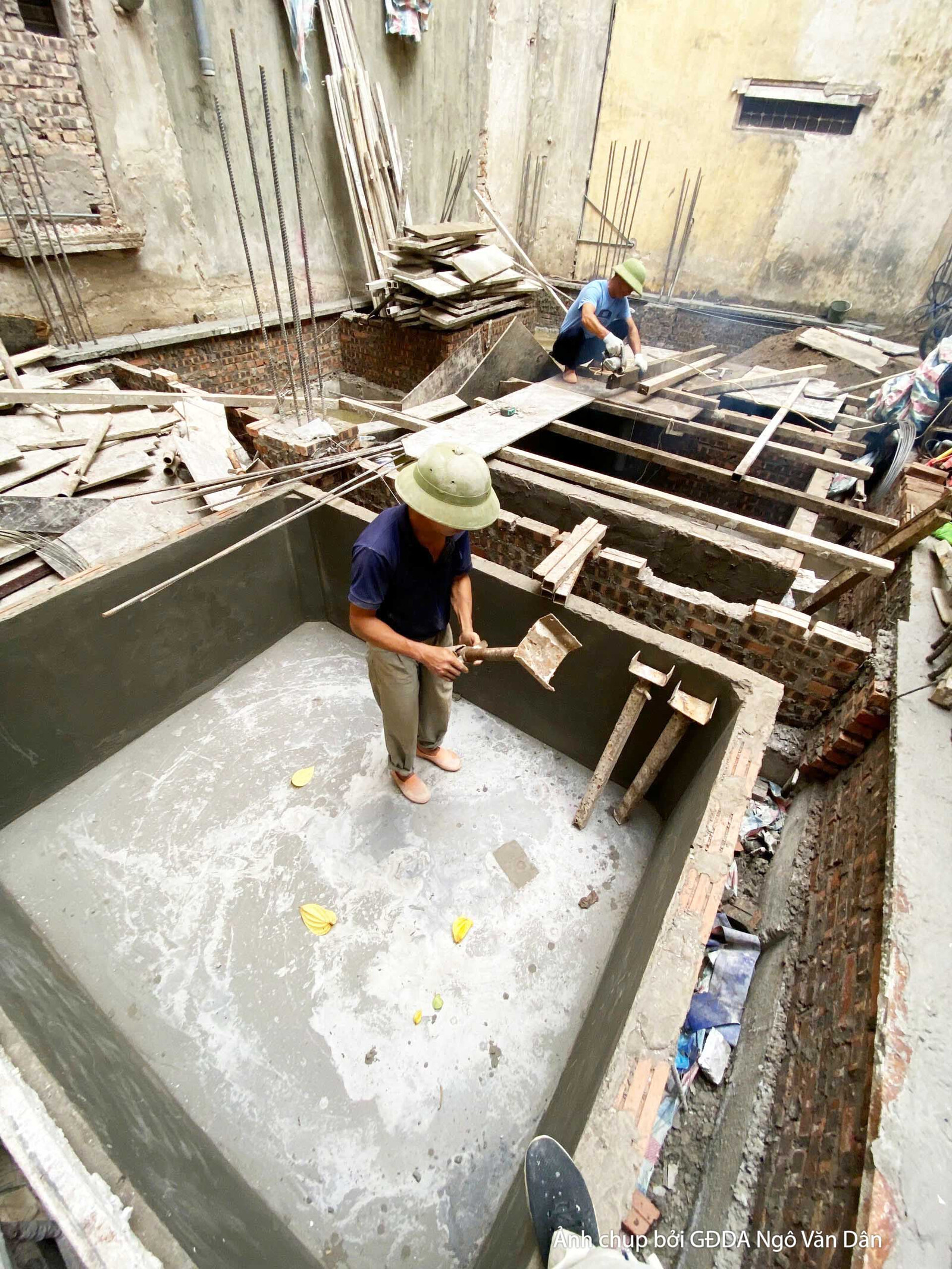 Sàn nhà đang trong quá trình đổ bê tông và san phẳng. Một công nhân đang làm việc trong không gian còn ngổn ngang vật liệu…