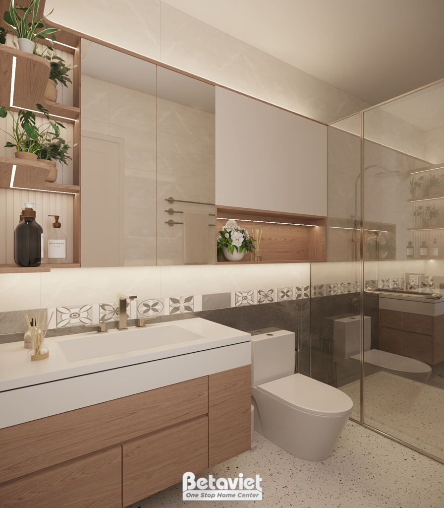 Cận cảnh khu lavabo phòng tắm, gương lớn phản chiếu kệ gỗ trưng bày cây xanh, mặt đá trắng và tủ gỗ vân nâu, viền tường ốp…