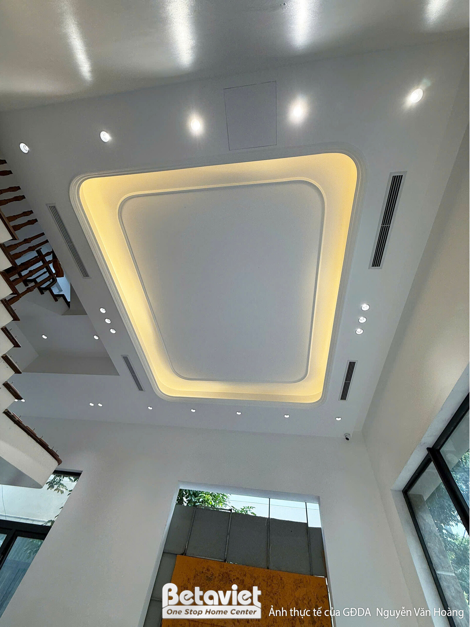 Trần nhà với đèn trang trí lớn hình chữ nhật phát sáng vàng, đang trong giai đoạn hoàn thiện. Trần thạch cao giật cấp, tạo…