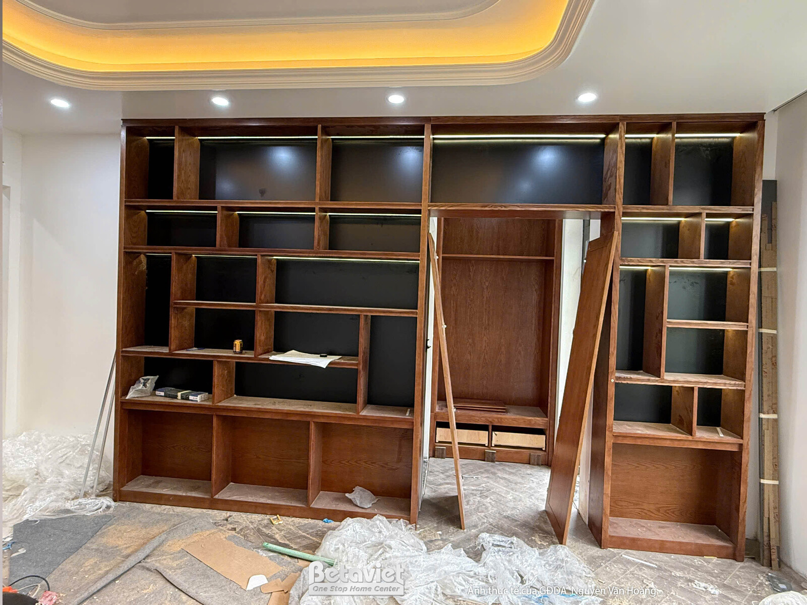 Không gian phòng chức năng đang lắp đặt hệ tủ gỗ lớn âm tường, nhìn cận cảnh hơn. Tủ gỗ màu nâu trầm với các khoang chứa đ…