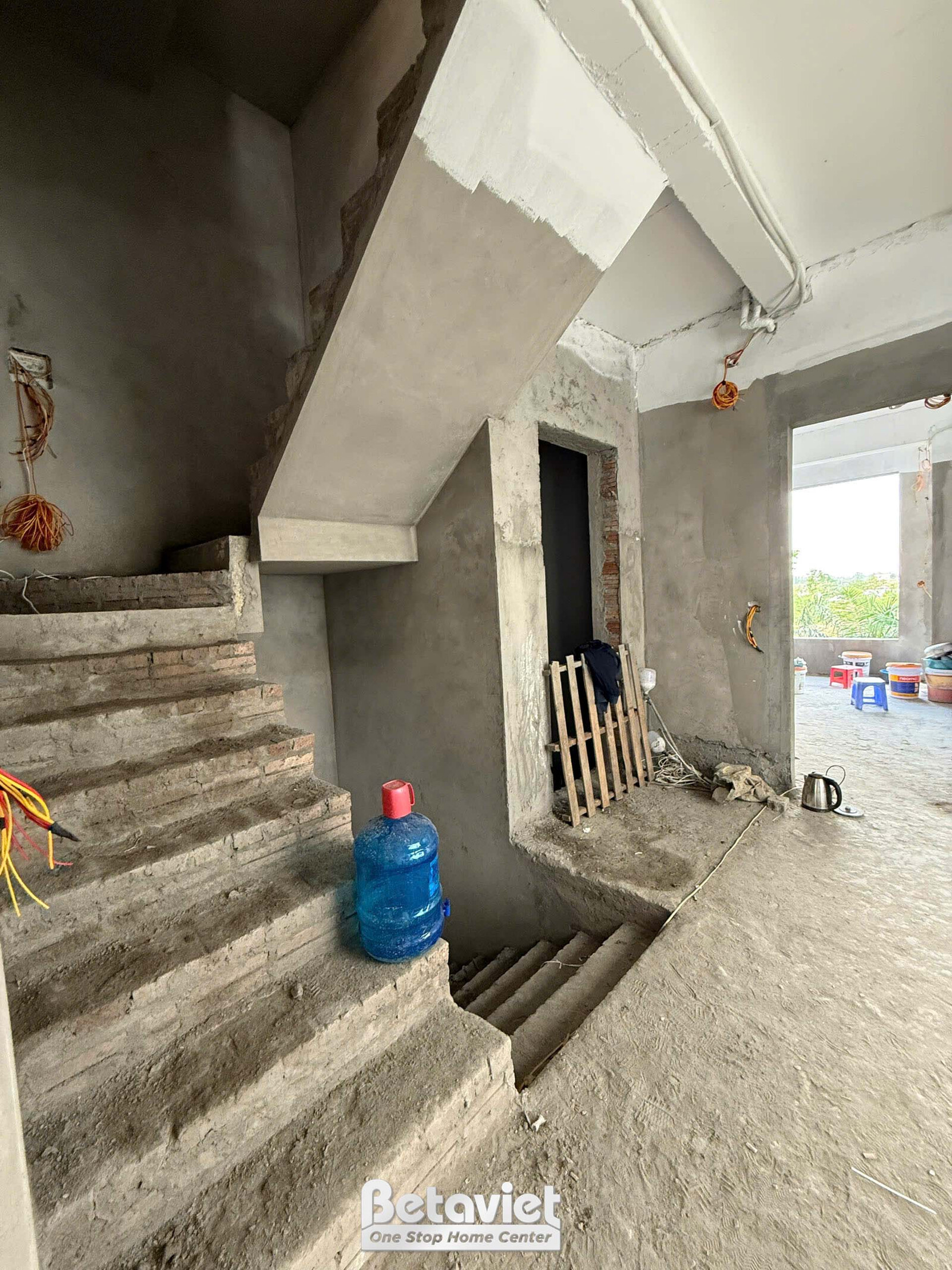 Góc nhìn từ chân cầu thang lên các tầng trên, đang trong giai đoạn phần thô. Cầu thang bê tông trần, tường bê tông chưa tr…