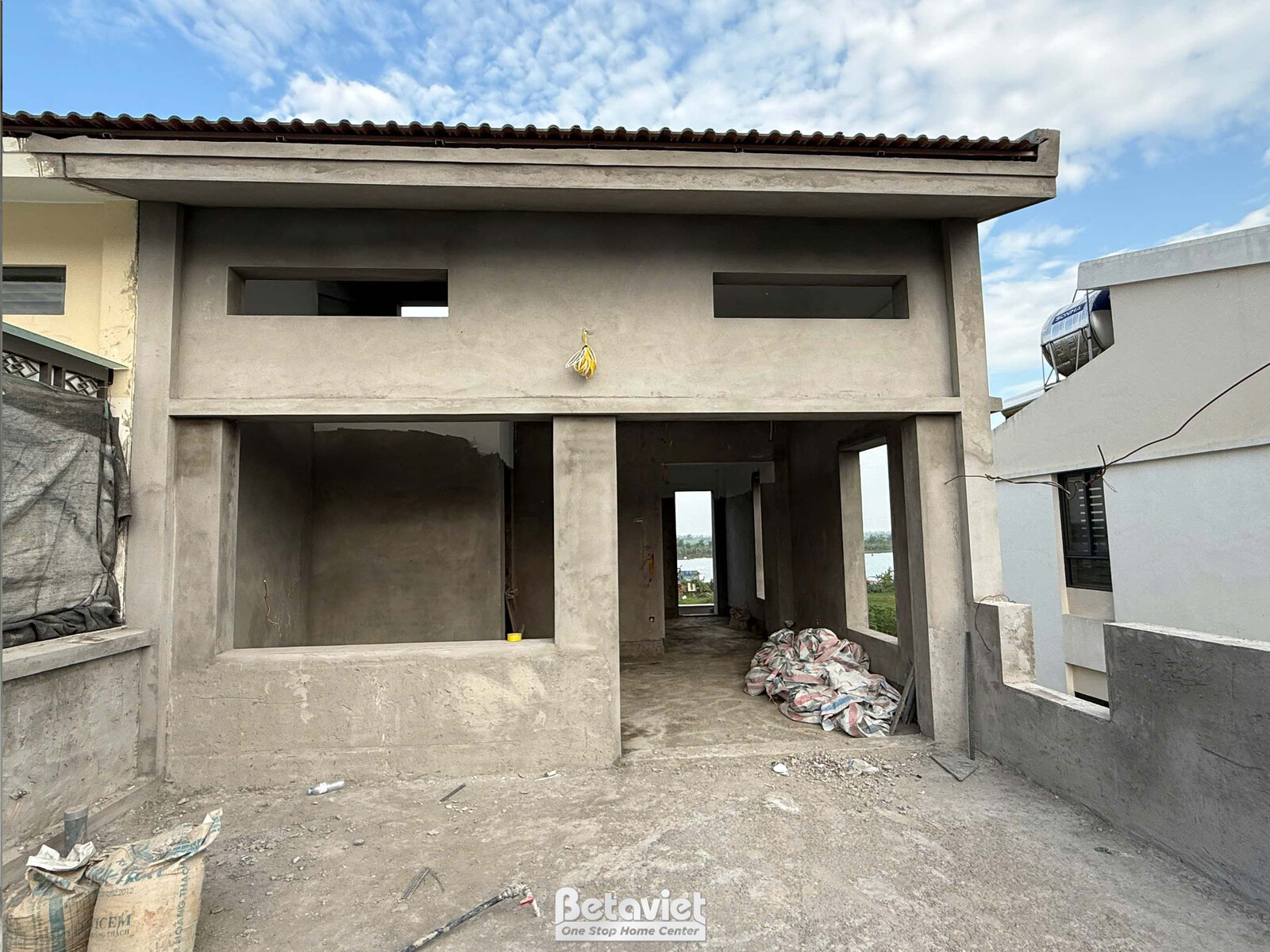 Sân sau hoặc khu vực phụ của nhà liền kề đang trong giai đoạn phần thô. Bề mặt đất chưa san lấp, tường bê tông trần và mái…