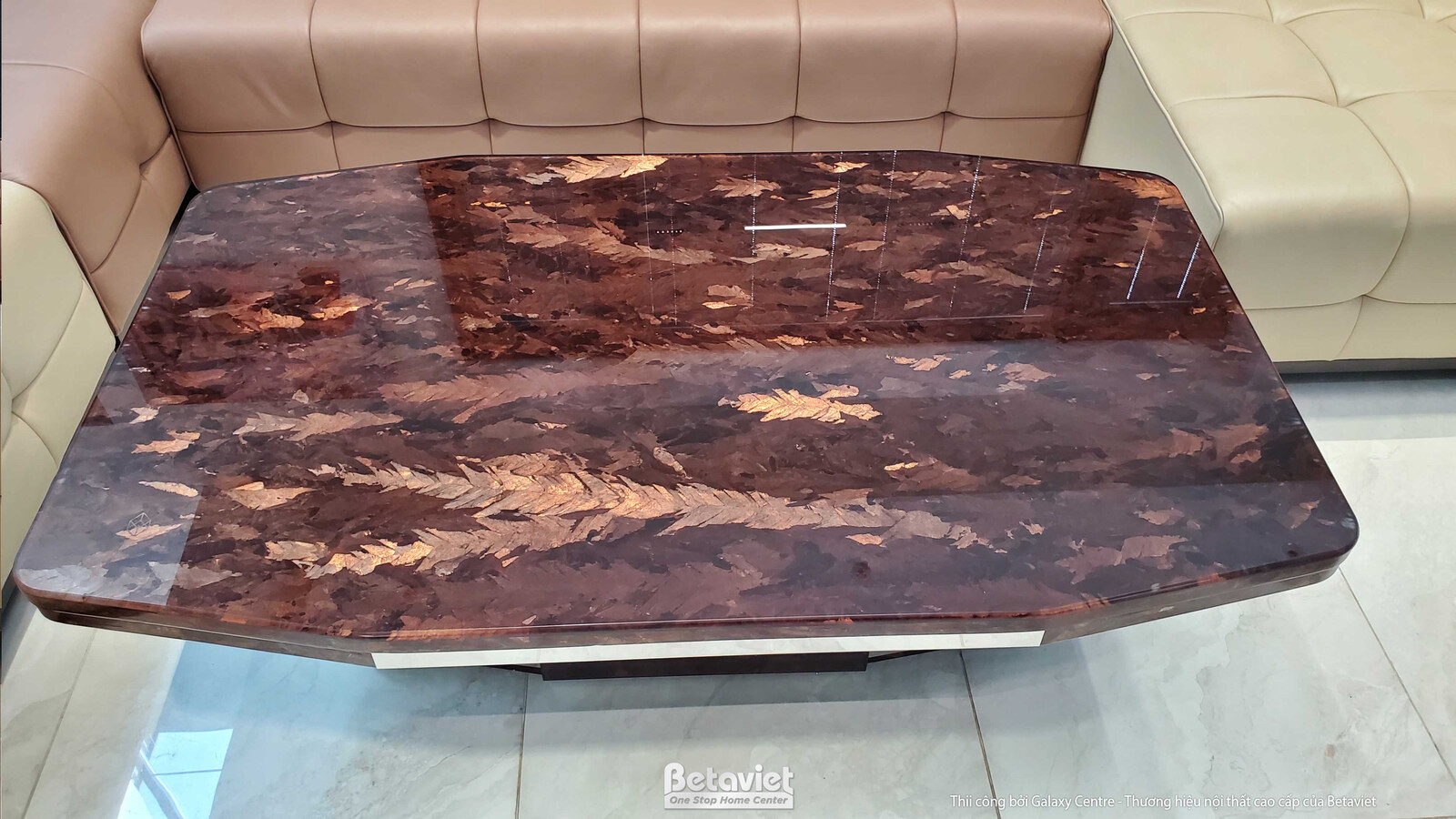 Cận cảnh bàn trà mặt đá vân nâu bóng với chân đế kim loại và gỗ, đặt trước bộ sofa màu be. Thiết kế hiện đại, tinh tế, là…