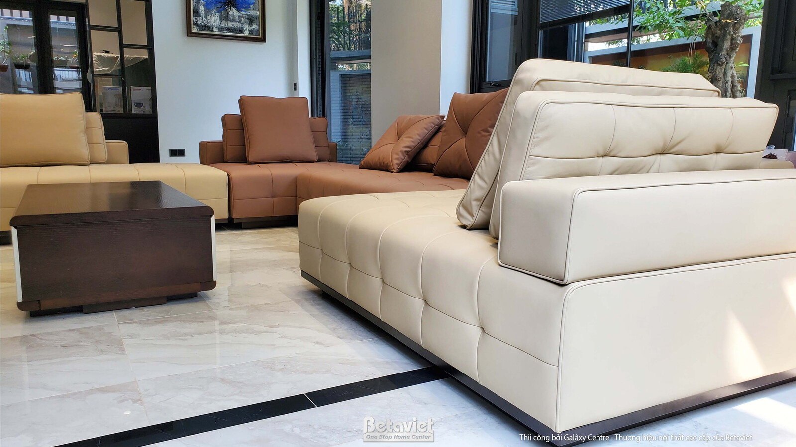 Chi tiết bộ sofa lớn màu be và nâu nhạt trong phòng khách, đặt trên sàn đá vân sáng. Bố cục mở, nội thất hiện đại, tạo cảm…
