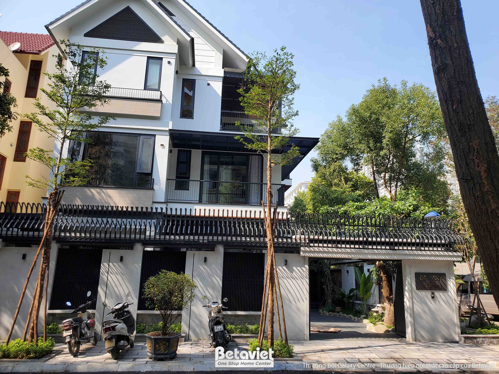 Toàn cảnh mặt tiền biệt thự hiện đại với kiến trúc khối hộp, mái dốc đặc trưng. Các mảng tường sáng màu kết hợp cửa kính l…