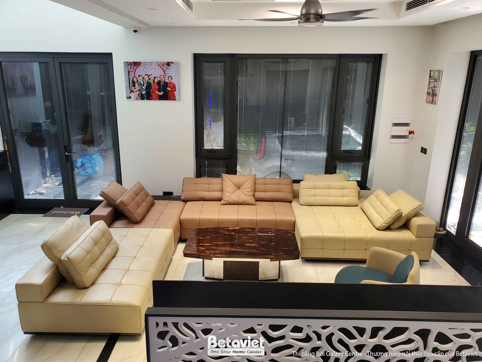 Phòng khách nhìn từ trên cao, bố cục sofa chữ L lớn màu be và nâu nhạt, bàn trà trung tâm. Trần thạch cao giật cấp, quạt t…