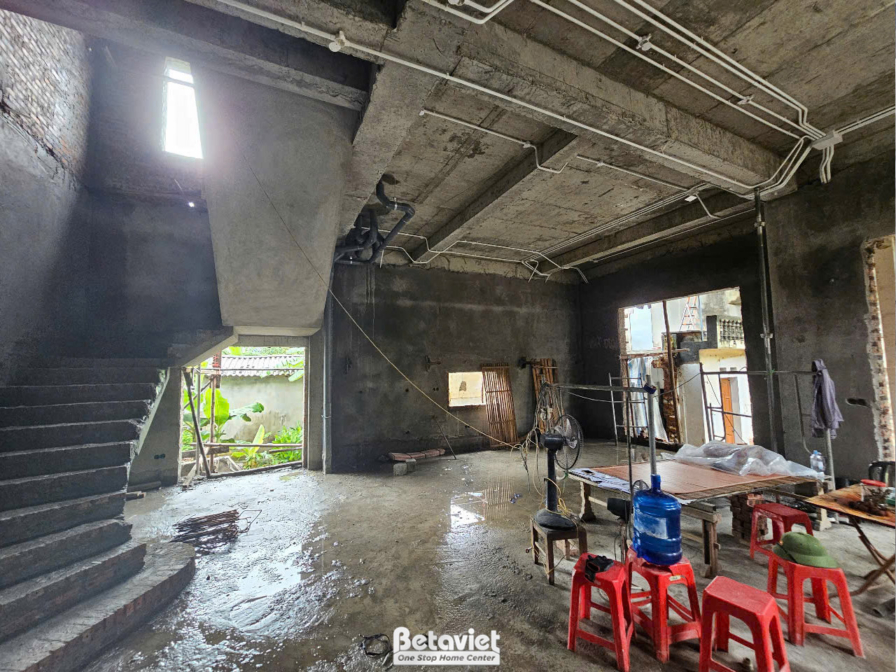 Không gian nội thất tầng trệt đang thi công phần thô, nhìn từ khu vực cầu thang. Sàn nhà còn ẩm ướt, tường và trần bê tông…