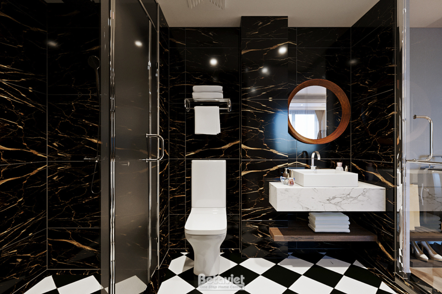 Góc khác phòng tắm suite Bay với lavabo đá trắng, bồn cầu, tường ốp marble đen vân vàng nổi bật. Gương tròn viền gỗ, sàn c…