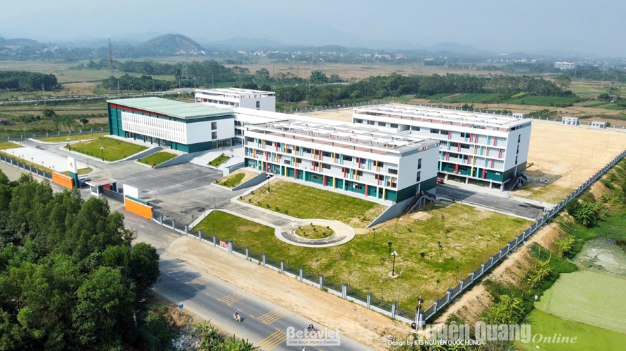 Ảnh flycam toàn cảnh khuôn viên trường sau hoàn thiện, các khối nhà trắng mái bằng nằm giữa nền đất và cánh đồng xanh, dãy…