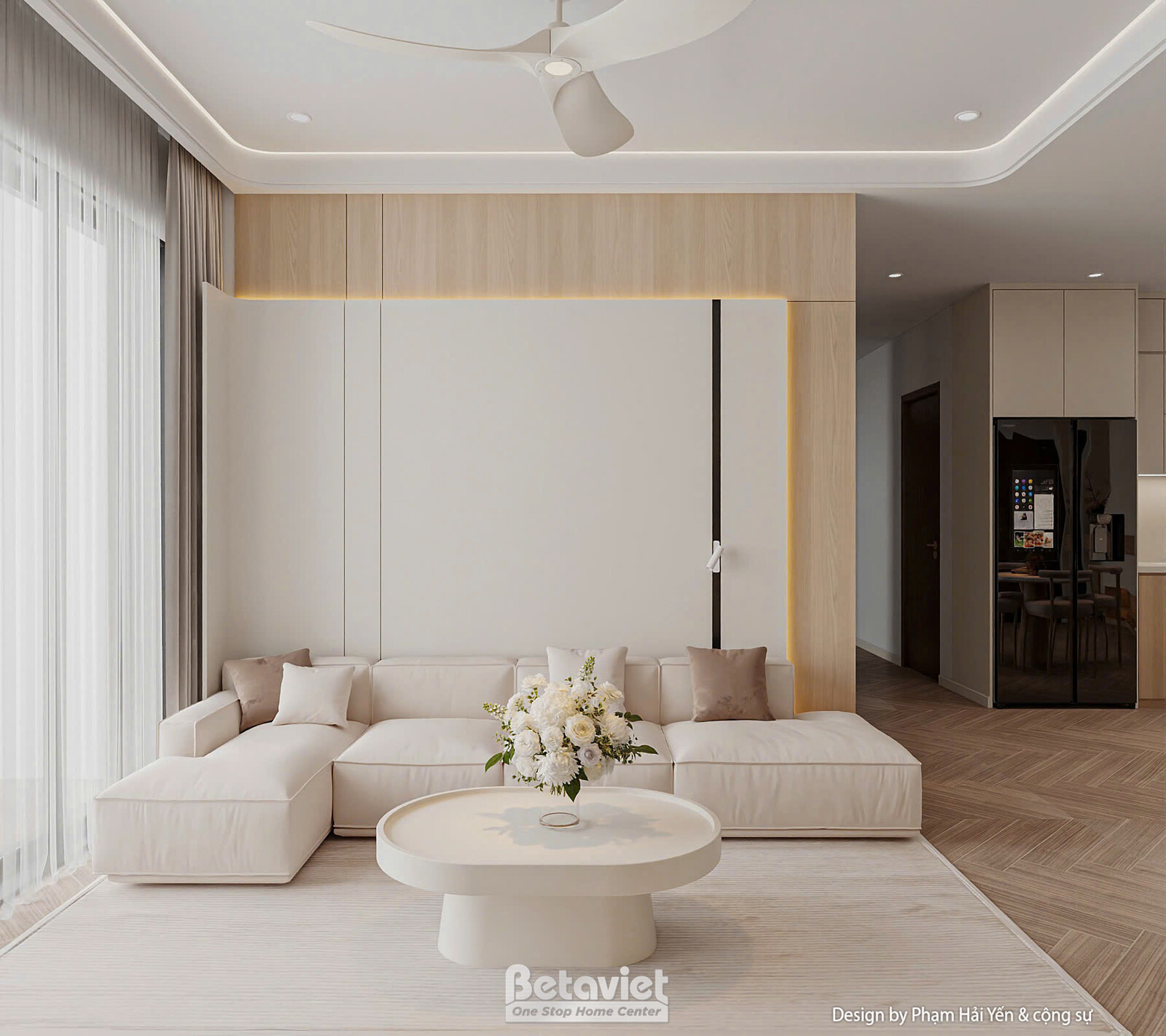 Góc rộng phòng khách với sofa chữ L bọc nỉ kem, gối tựa nâu nhạt, bàn trà tròn mặt đá điểm hoa trắng. Phía sau là hành lan…