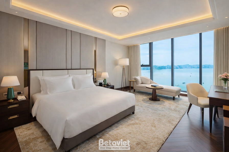 Phòng ngủ view vịnh biển đảo đá, giường lớn ga trắng, sofa thư giãn đặt cạnh cửa sổ, trần khung phào chỉ hắt đèn dịu, sàn…