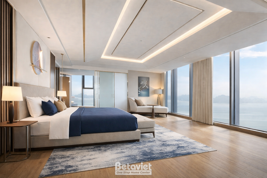 Phòng suite rộng thoáng, giường lớn ga xanh navy, khu tiếp khách sofa bố trí riêng biệt, trần giật cấp đèn hắt, cửa kính l…