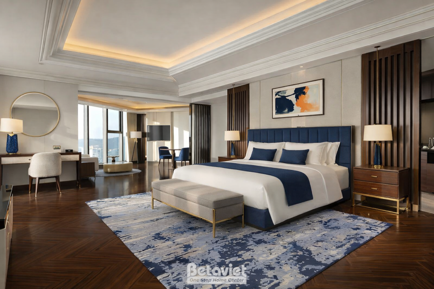 Suite có khu làm việc tiếp khách riêng, giường lớn đầu giường xanh navy, sàn gỗ xương cá tối màu, tranh trừu tượng cam xan…