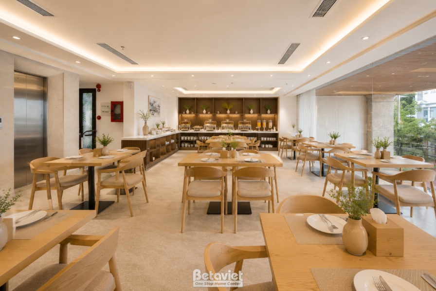 Không gian nhà hàng nhìn về phía quầy buffet và khu thang máy, kệ gỗ nan trưng bày món ăn, cột ốp đá điểm nhấn. Bàn ghế gỗ…